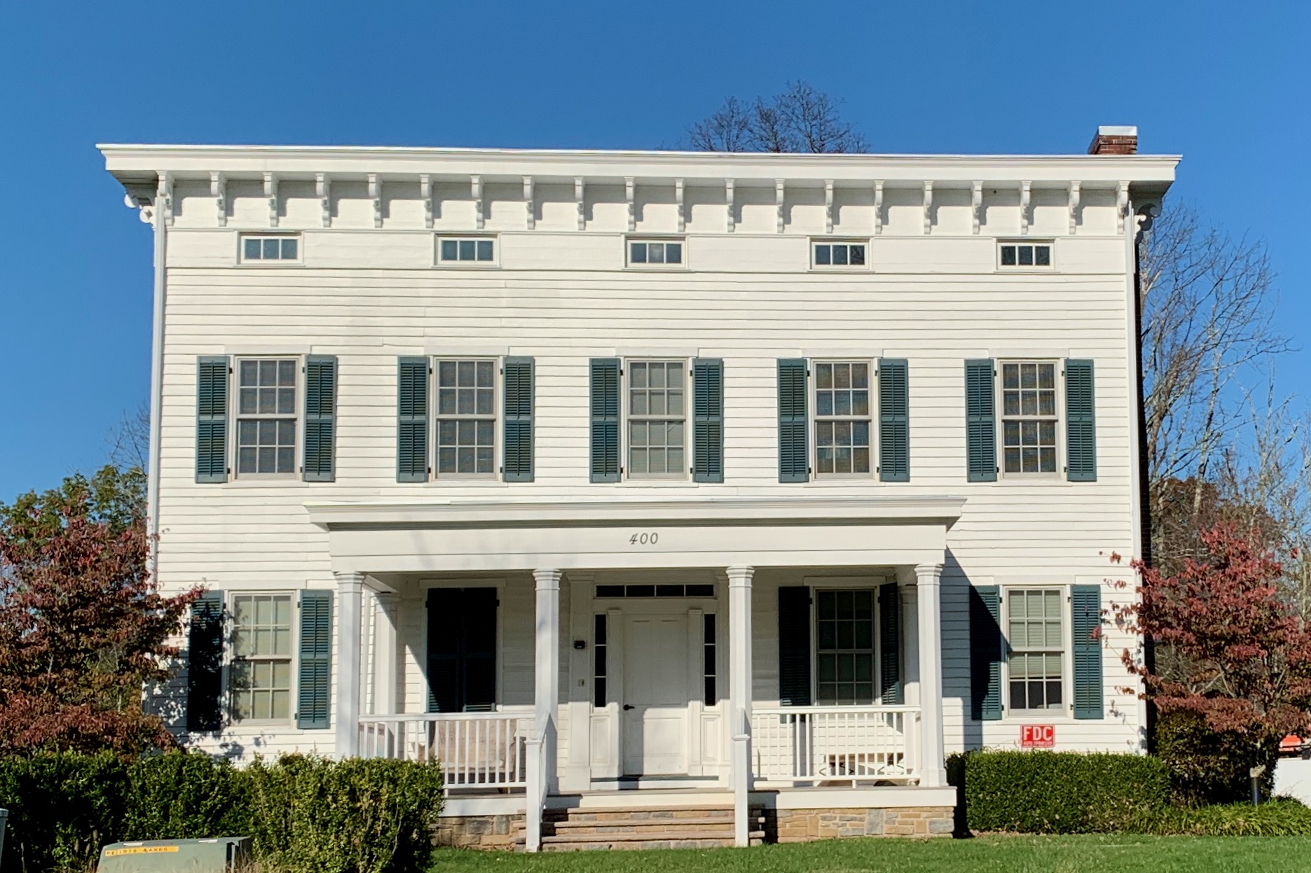 White clapboard building with dark green shutters, a columned porch, and the number 400 over the door